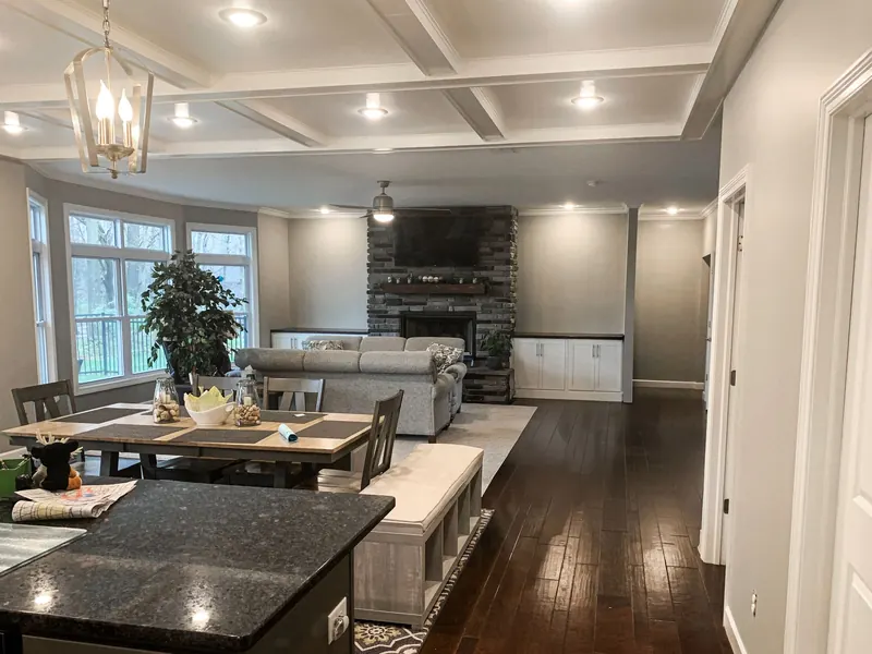 Open-concept home interior featuring a dining area, a living room with a stone fireplace, and dark wood flooring.