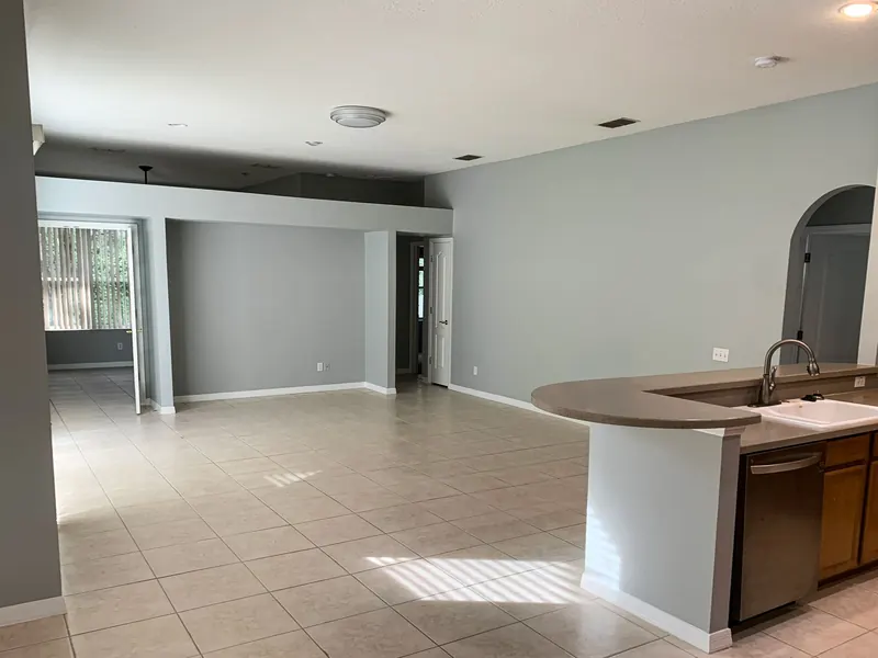 An open-concept living area with gray walls, light tiled floors, and a kitchen island with stainless steel appliances.