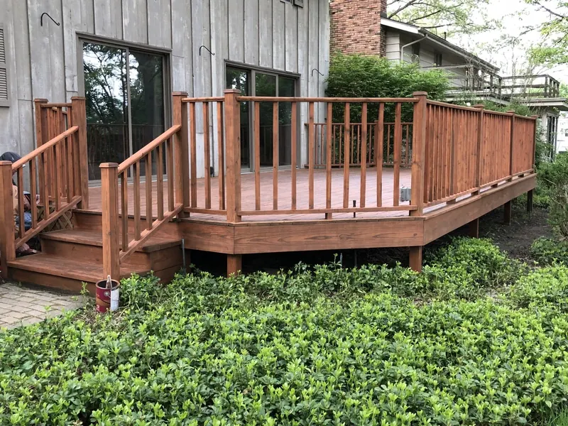A medium-brown wooden deck with railings and steps leading to a glass sliding door on a house exterior.