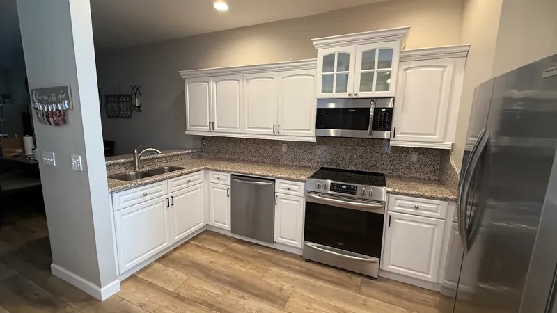 Kitchen with white shaker cabinets, granite countertops, and stainless steel appliances after cabinet refinishing.