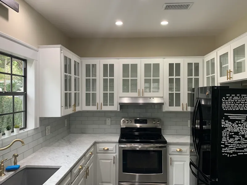 Bright kitchen with white glass-front upper cabinets, gray subway tile backsplash, and a stainless range.