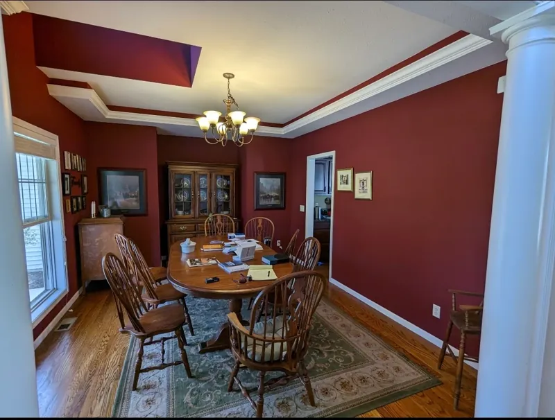 Formal dining room with deep red walls, white trim and columns, a chandelier, and a wood dining set.