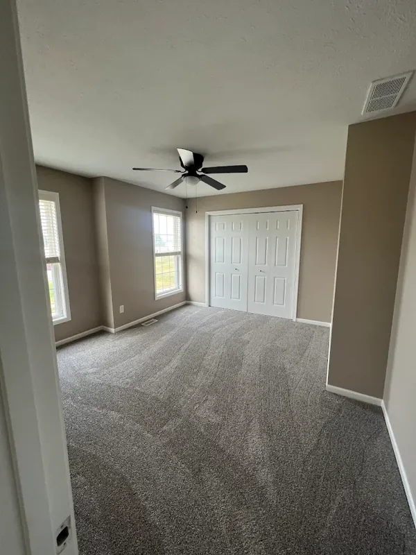Freshly painted empty bedroom with warm gray walls, white trim, a ceiling fan, and new carpet.