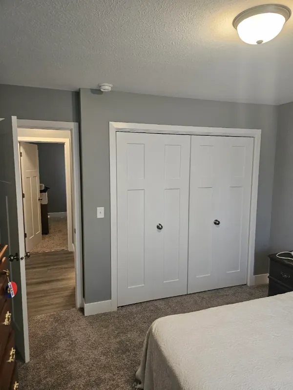 Bedroom with soft gray walls, white bifold closet doors, and white trim.