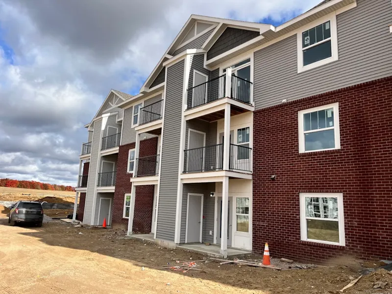 Three-story apartment building with gray siding, red brick accents, and balconies during a new construction paint job.
