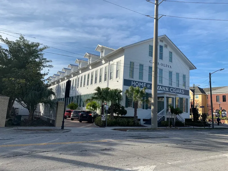 White two-story historic commercial building with a wraparound balcony and palm trees.