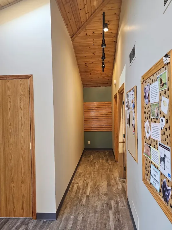 Hallway with white walls, a wood-plank ceiling, and a bulletin board.