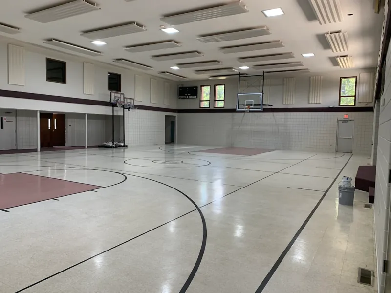 Indoor basketball gym with white walls, a polished wood court, and basketball hoops.