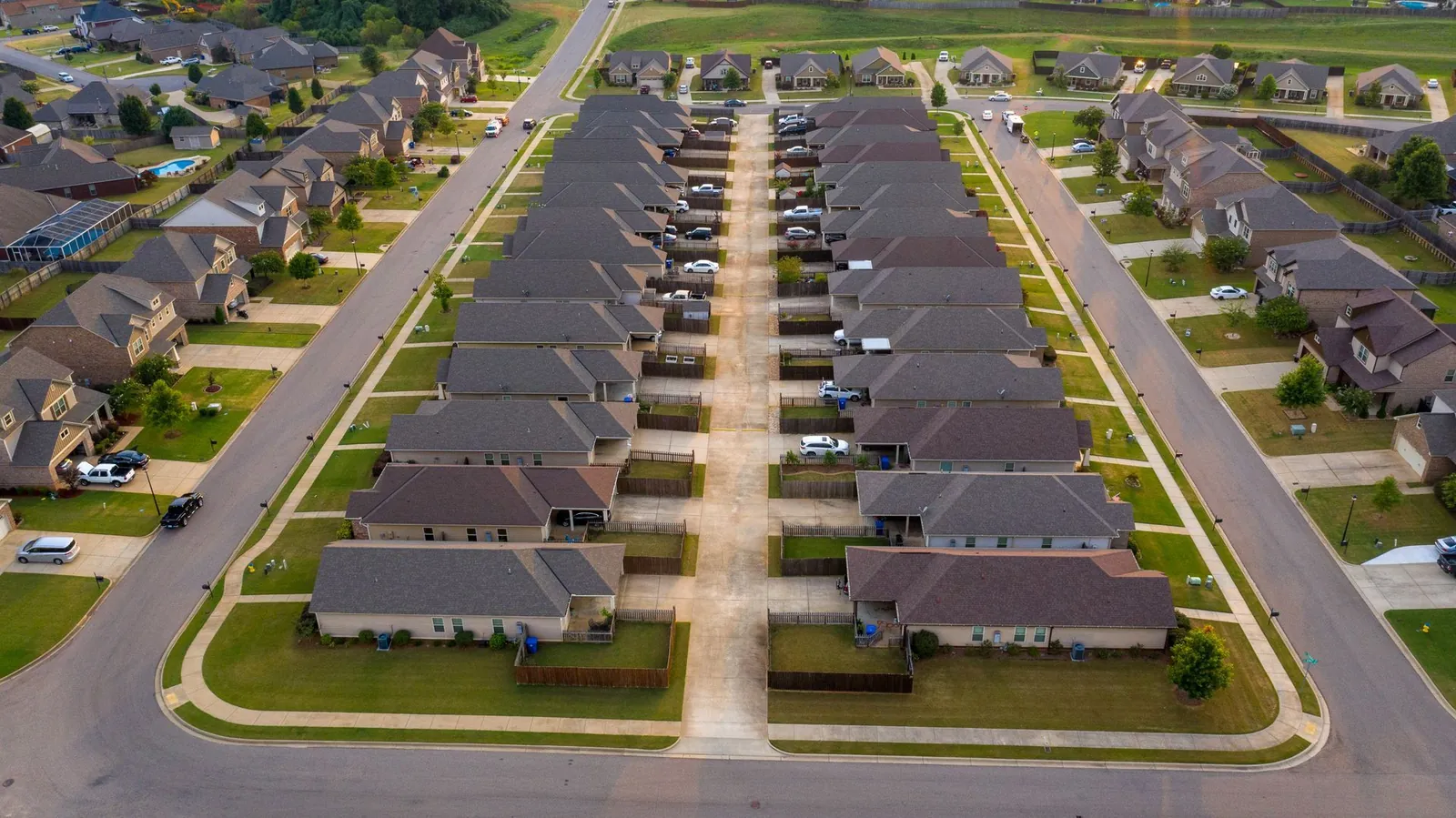 Aerial view of a suburban neighborhood featuring rows of single-story houses with gray roofs along a central concrete alley.