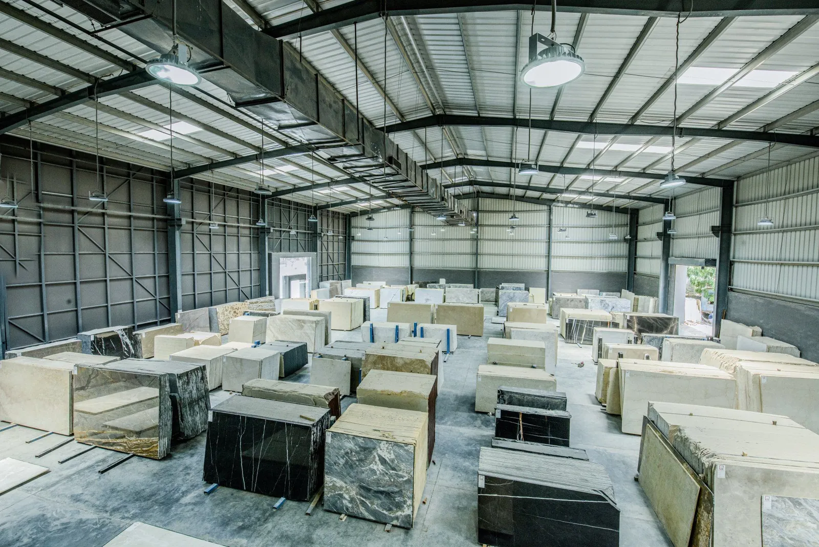 Warehouse interior filled with rows of stacked stone and marble slabs under industrial lights.