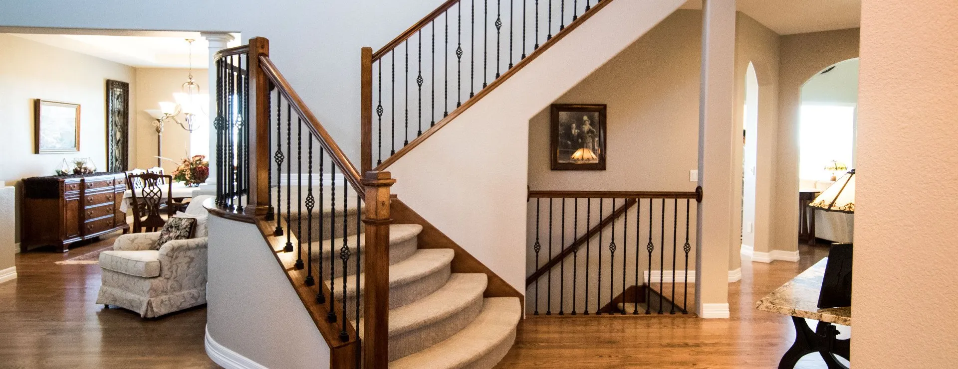 A grand foyer featuring a curved staircase with carpeted steps and dark wood railings, leading into an open living space.