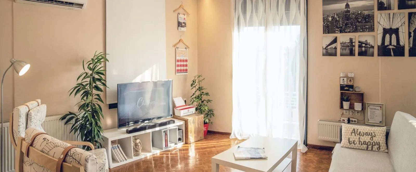 A cozy living room with a TV on a white stand, a coffee table, indoor plants, and a sofa with a decorative pillow.