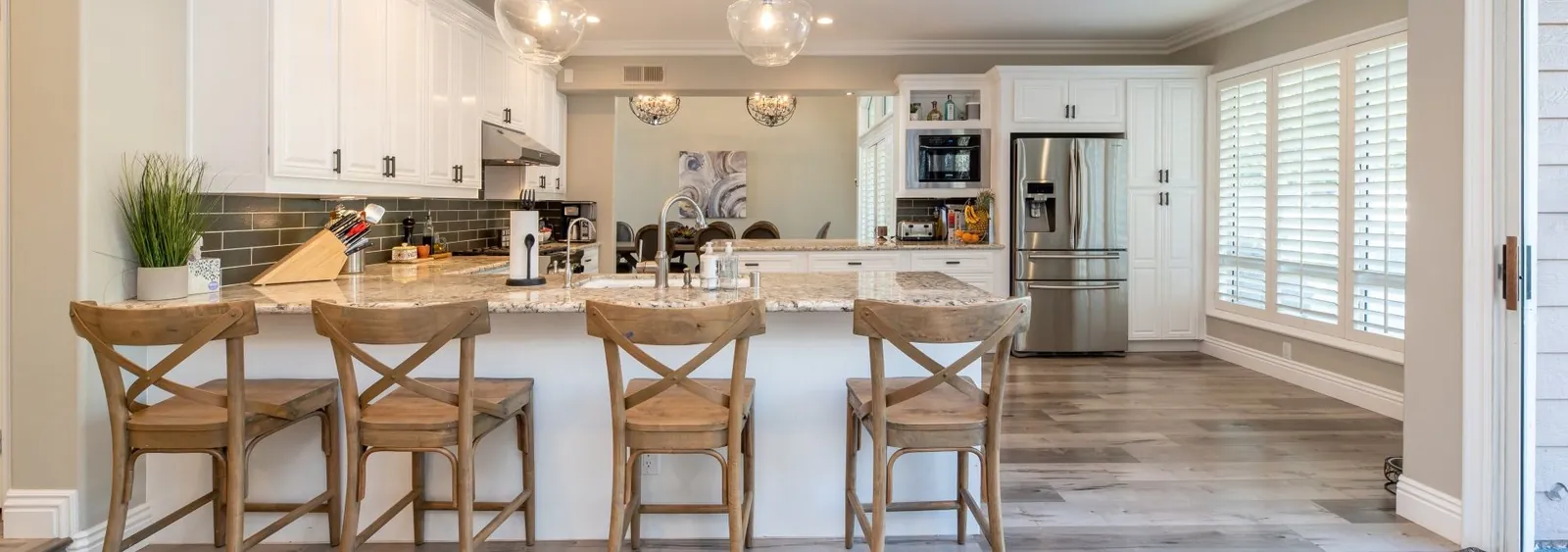 A kitchen features a white island with four wooden stools, light-colored countertops, and white cabinetry.